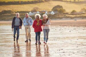 Group of smiling senior friends walking arm in arm along shoreline of winter beach