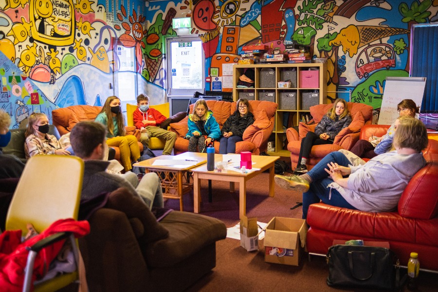 Young people sat in brightly coloured room on sofas, listening to researchers