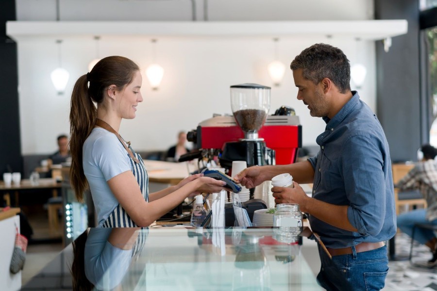 Man buying a cup of coffee to go and making a contactless payment at a coffee shop