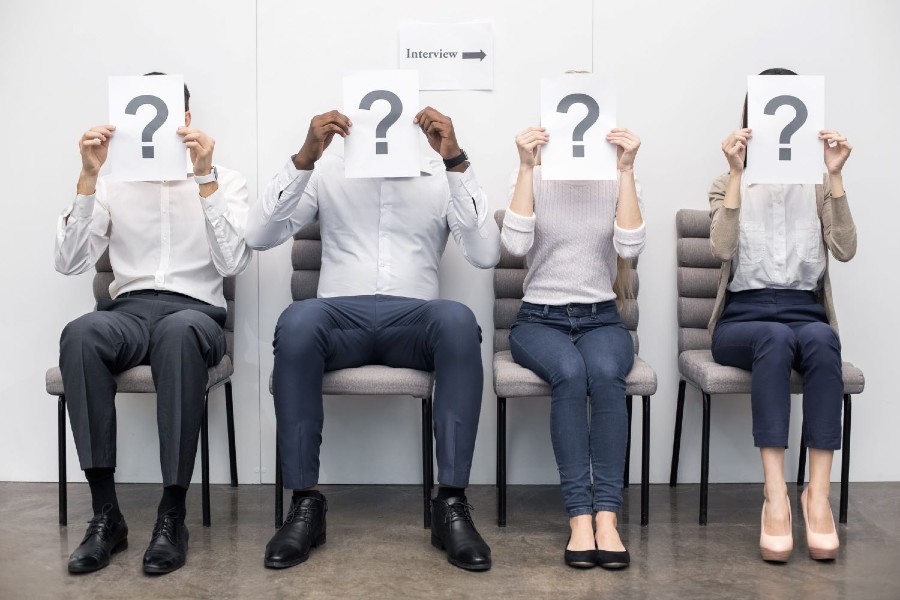 People sitting waiting for a job interview holding up a question mark.