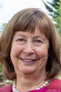 Portrait photo of Lisa Hall. She has shoulder length brown hair with a fringe. She's wearing a pearl necklace and pink top. 