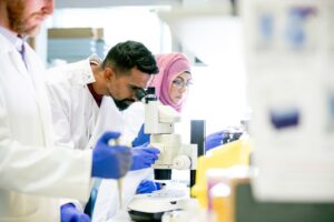 A small group of scientists run tests in a state of the art laboratory; they are all wearing surgical gloves and lab coats