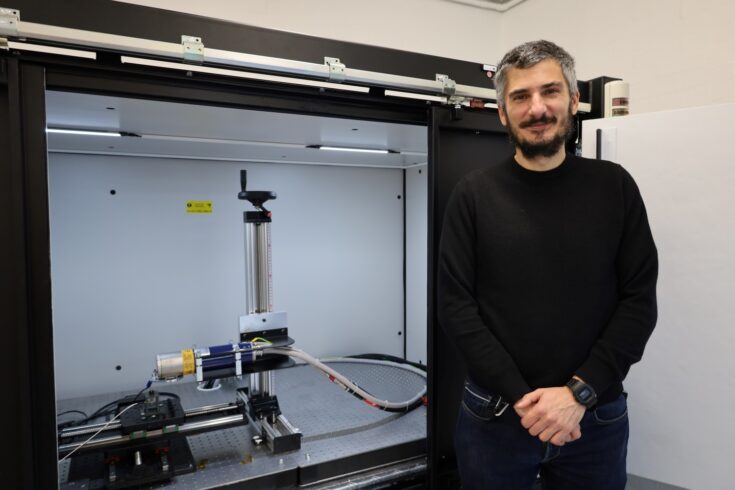 Man stood in front of a black cupboard with a clear front panel, inside is a piece of scientific equipment 