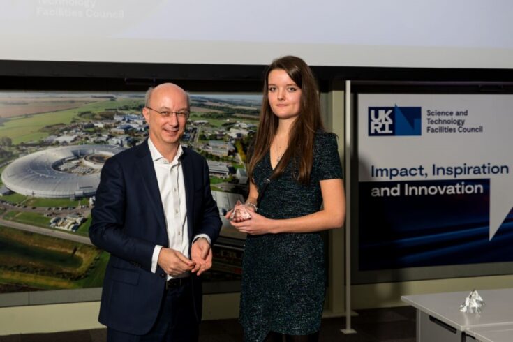 A man and a woman smiling. The woman is holding an award that she has won. 