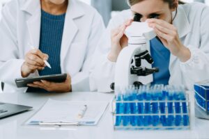 Two scientists meeting in a lab, looking through a microscope and writing notes.