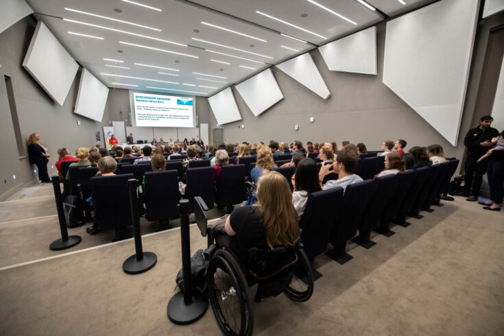 Attendees sitting in a lecture theatre watching a panel discussion at an MRC Human Genetics Unit internal event called ‘Shining a light on rare genetic disease’