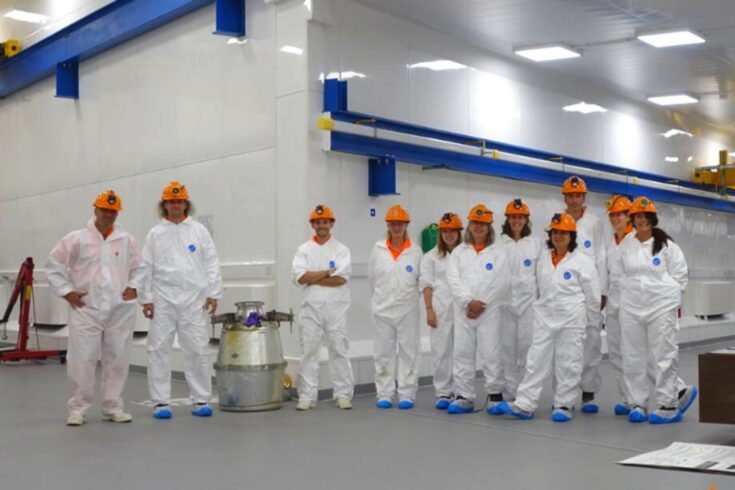 A group photo of a team wearing hard hats and overalls in a lab