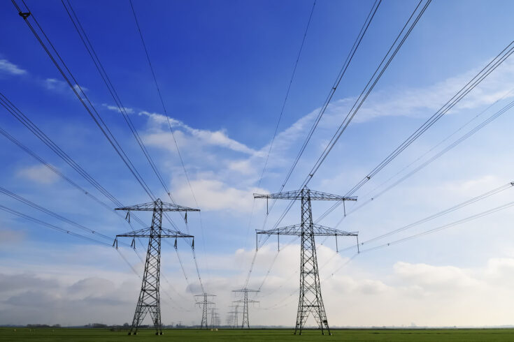 Silhouettes of power lines in a flat landscape and blue sky.