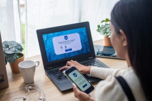 A young woman at a desk using two-factor authentication on her phone and laptop.