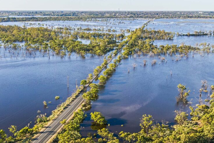 Aerial view of flooded tree-lined Bookpurnong Road, the main Loxton to Berri connector road on River Murray in South Australia: flooded Gurra Gurra floodplain, bridge over Gurra Gurra Creek in centre frame, town of Berri in the distance on tree-covered hills, River Murray just visible in distance.