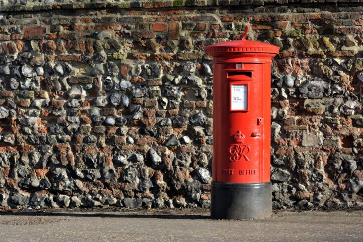 Red post box in front of a brick wall