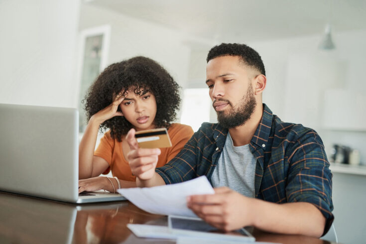 Shot of a stressed out young couple using a credit card while going over their finances at home.