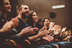 A row of people sitting in an audience, smiling and clapping.