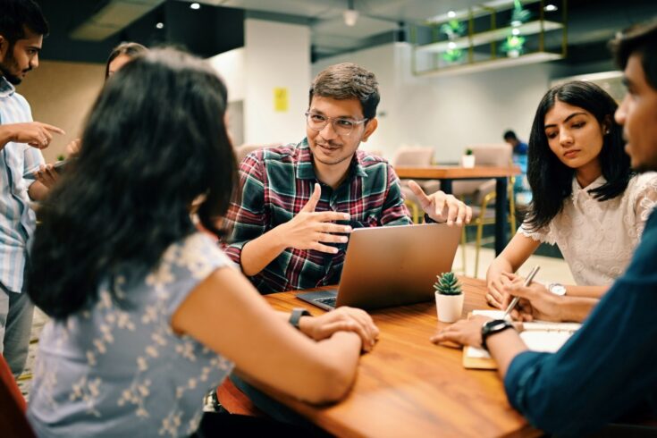 A group of people with laptop and notebook talking to each other around a table