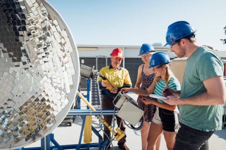 A group of people with blue safety helmets learning about solar dishes