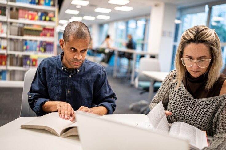 Visually impaired man reading a braille book in university library